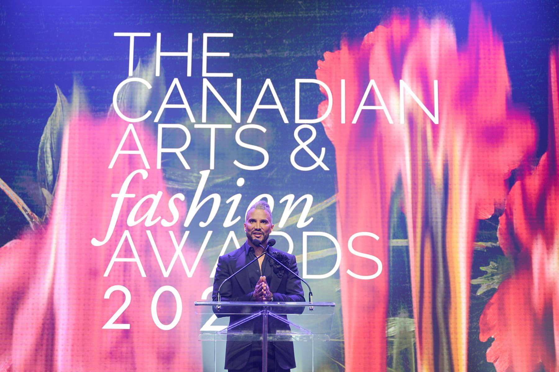 Host at the podium in front of the Canadian Arts & Fashion Awards stage screen