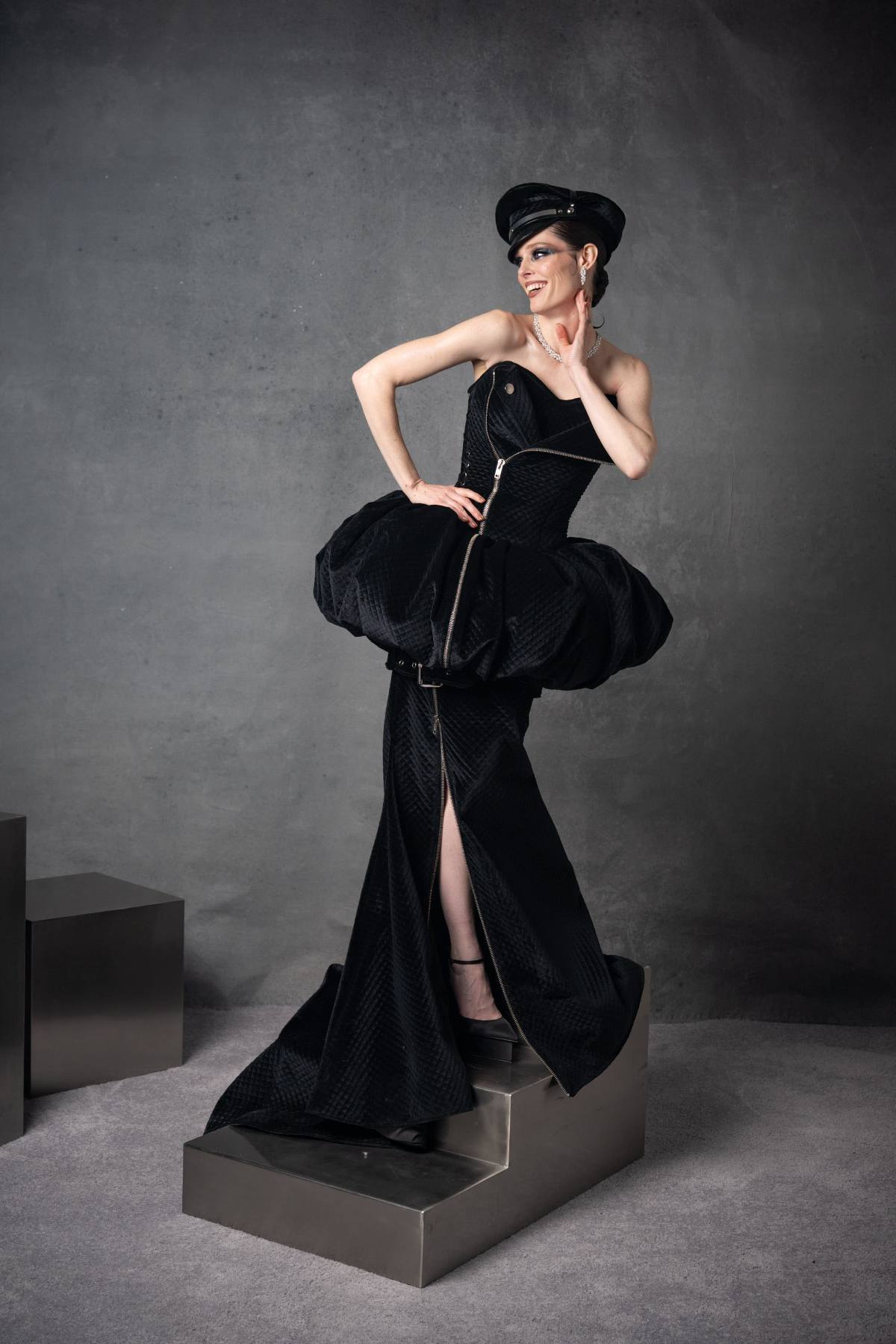 A performer in a sculptural black gown posed on a plinth