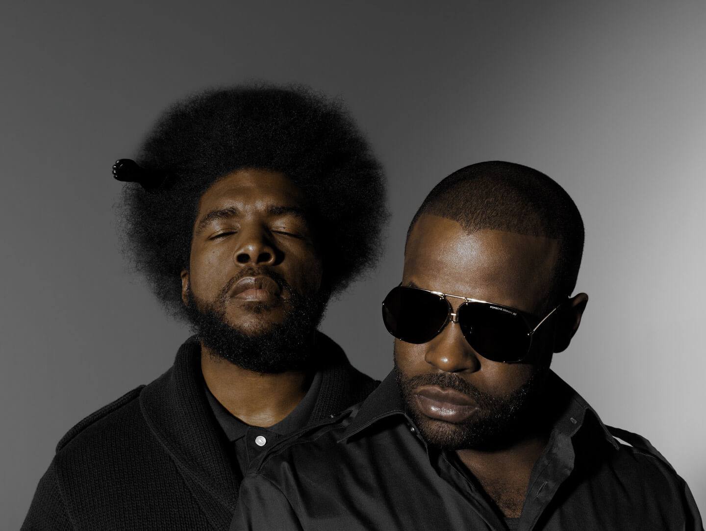 Two musicians photographed together against a grey backdrop