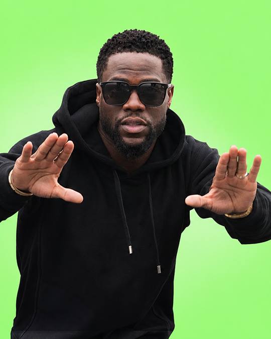 A comedian in sunglasses posing against a green backdrop
