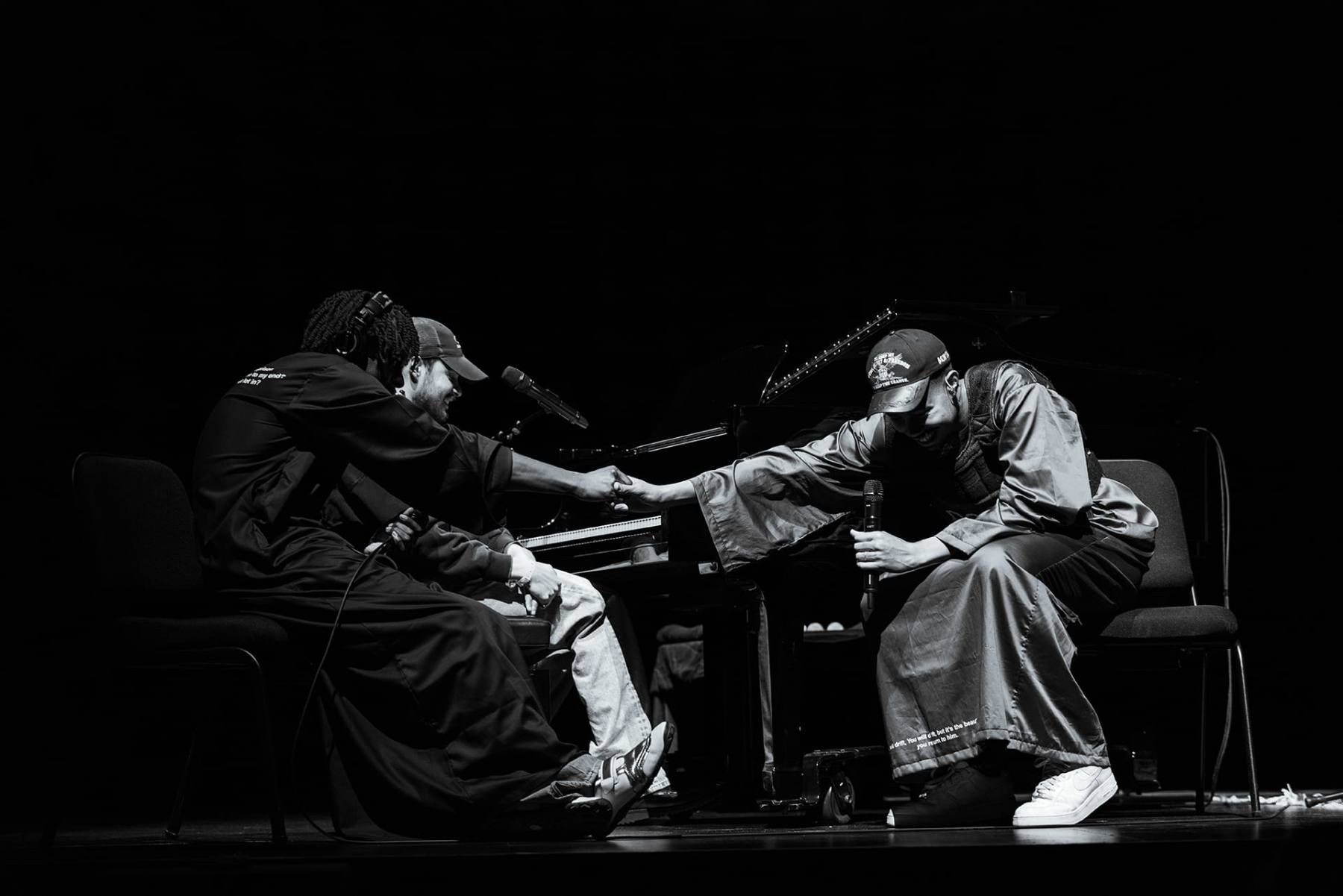Performers greeting each other on stage beside a piano