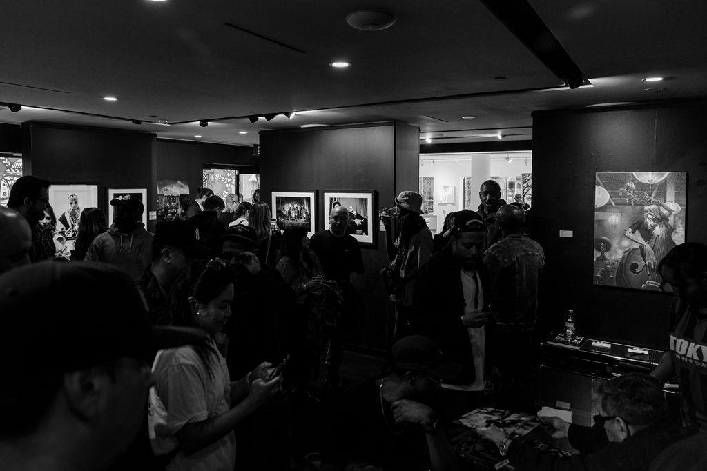 A crowded gallery opening with framed artworks on the walls